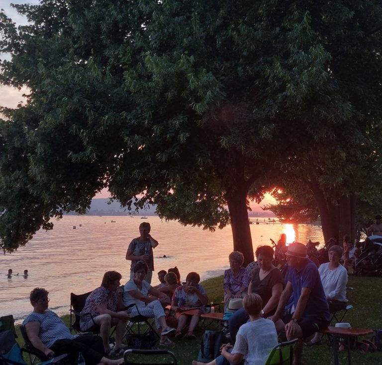 Veranstaltungsfoto. Abgebildet ist das Publikum. Im Hintergrund ist der Bodensee im Abendrot.