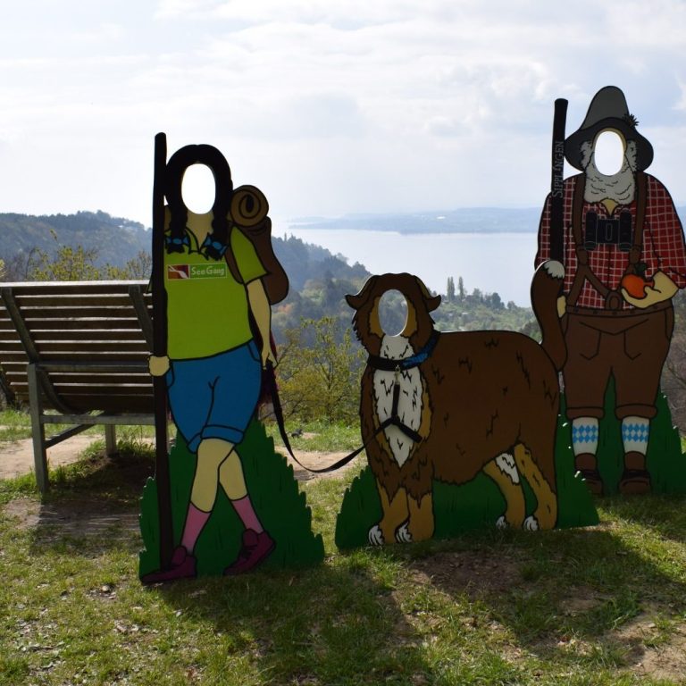 Fotowand, bei der Wanderer ihre Gesichter durchstrecken können. Ergibt lustige Fotos vor einer wunderschönen Bodenseelandschaft.